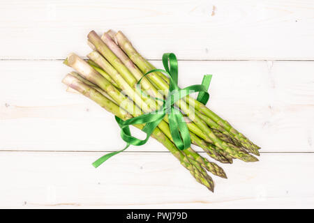 Bundle di sacco di intere fresche asparago verde lancia legati dal nastro verde flatlay su legno bianco Foto Stock