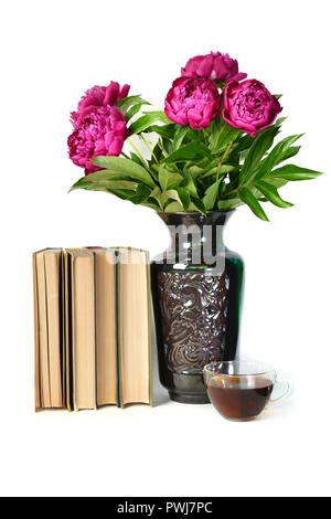 Bellissimo il lilla le peonie in un vaso, una tazza di tè e un libro su un isolato bianco sullo sfondo. Foto Stock