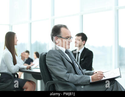 Malinconici imprenditore maturo in tuta con il suo team di lavoro dietro Foto Stock