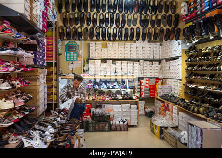 YAZD, IRAN - Agosto 18, 2016: vecchio mercante iraniani la vendita di scarpe leggere il giornale in Farsi in Yazd Bazaar di Khan. Yazd è una delle principali città del cen Foto Stock