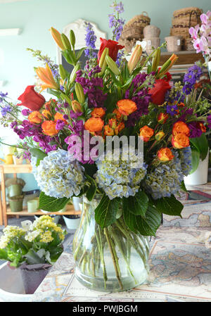 Foto di una lussureggiante floreale in un chiaro vaso di vetro. Ortensia, rose, gigli, spray rose, stock, larkspur, ecc. Foto Stock