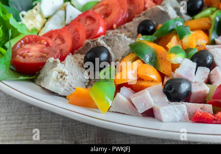 Un famoso piatto della cucina americana - insalata Cobb, costituito da verdi, uova, pomodori, formaggi, prodotti a base di carne, impilati in fila su di un ampio piatto e poure Foto Stock