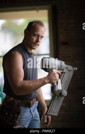 Ritratto di un builder maschio utilizzando un utensile di potenza all'interno di una stanza che egli sta lavorando a. Foto Stock