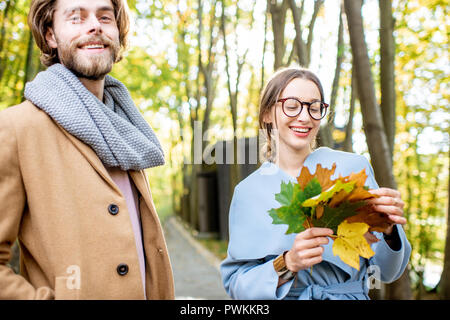 Giovane coppia elegante vestito di cappotti in piedi con foglie all'aperto nella foresta Foto Stock