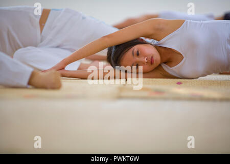 La teenager fare yoga si estende con un gruppo di donne in una classe. Foto Stock