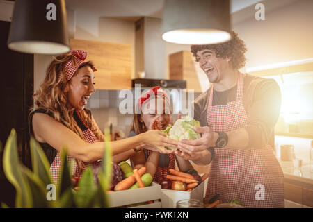 Carino bambina e la sua bella i genitori sono il taglio di vegetali e di sorridere mentre rendendo pickle in cucina a casa Foto Stock