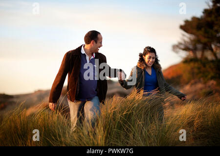 Felice metà adulto giovane tenendo le mani mentre si cammina attraverso erba lunga. Foto Stock