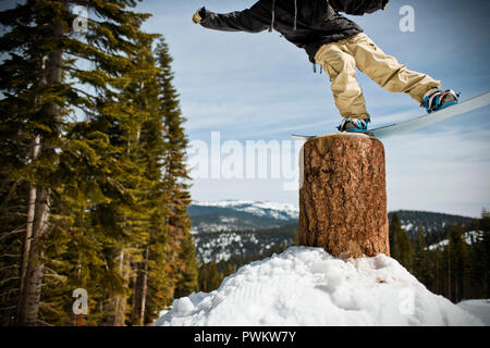 Giovane uomo in equilibrio su un ceppo di albero con il suo snowboard mentre all'aperto nella neve. Foto Stock