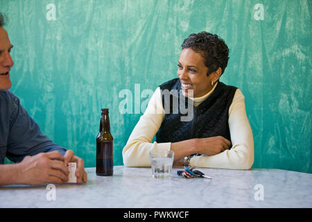 Sorridente metà donna adulta la condivisione di un drink con un amico maschio a una tabella. Foto Stock