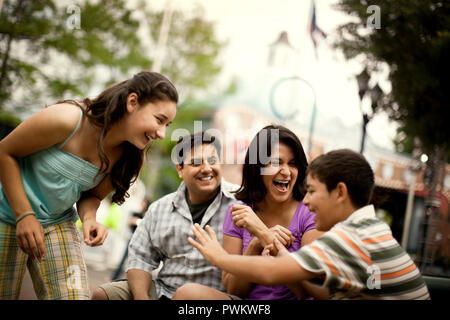 Ridendo famiglia seduta su una panchina in un parco di divertimenti. Foto Stock