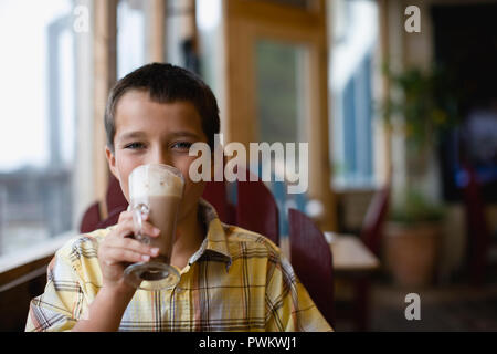 Ritratto di un ragazzo beve una cremosa bevanda al cioccolato. Foto Stock