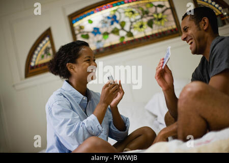 Ridendo coppia giovane giocare con carte mentre seduta con le gambe incrociate sul loro letto. Foto Stock