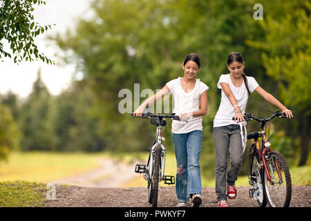 Due ragazze godere spingendo le loro biciclette su strada di ghiaia. Foto Stock