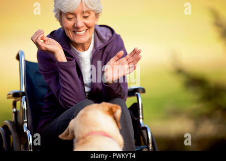 Sorridente donna senior in una sedia a rotelle guardando il suo cane. Foto Stock