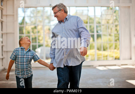 Ragazzo giovane e suo nonno tenendo le mani mentre grinning all'altra all'interno di un garage. Foto Stock