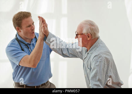 Senior uomo dando un infermiere maschio ad alta cinque all'interno di una stanza. Foto Stock