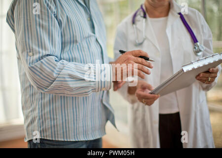 Le mani di un medico donna tenendo un clipboard accanto ad un collega di sesso maschile in possesso di una penna. Foto Stock