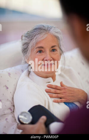 Speranzoso senior donna guardando un infermiere, pur avendo la sua pressione del sangue preso. Foto Stock