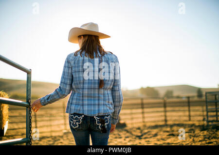 La moglie di un agricoltore che indossa un cappello da cowboy l'apertura di un cancello fuori del ranch. Foto Stock