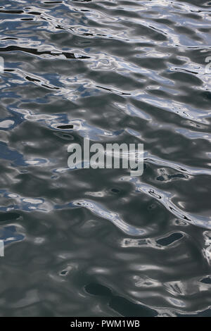 Full-frame abstract di dolci onde sulla superficie del mare come visto da sopra e con un sacco di riflessioni di cielo blu e nuvole bianche; buona per lo sfondo. Foto Stock