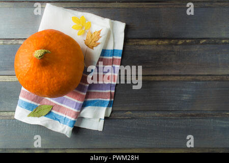 La zucca arancione con il tessuto e caduta foglie grigio su un tavolo di legno con lo spazio di copia Foto Stock