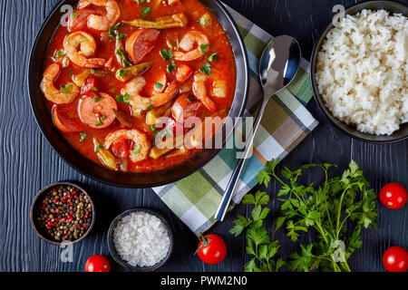 Vista aerea del delizioso gumbo con gamberetti, okra e salsiccia in una ciotola su una tavola nera con igienico e cucchiaio d'argento, vista da sopra, close-up, fl Foto Stock