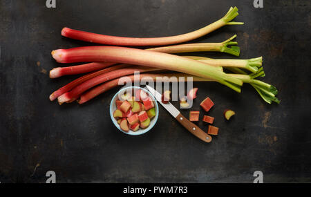 Steli di rabarbaro e di rabarbaro tagliato in una ciotola con un coltello Foto Stock