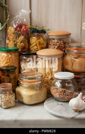 Ancora vita disposizione in una dispensa di vasetti di archiviazione del passato, dadi, marmellate, olive, frutta e le lenticchie in una dispensa su un ripiano di marmo Foto Stock