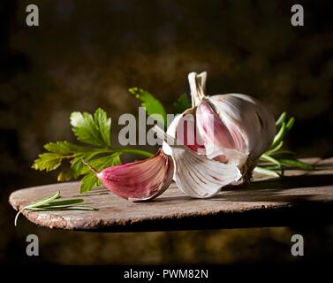 Un bulbo di aglio e il prezzemolo su una tavola di legno Foto Stock