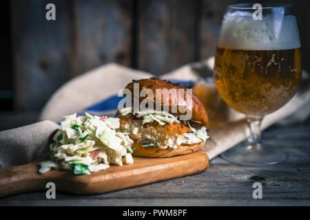 Un rustico hamburger di pesce con coleslaw e birra Foto Stock