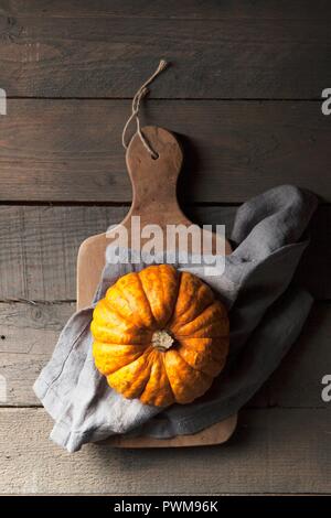 Una zucca munchkin su un rustico in legno con sfondo grigio di un tovagliolo di lino Foto Stock