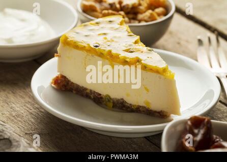 Una fetta di mascarpone e yogurt greco cheesecake con una data e una base in legno di noce, guarnita con maracuja Foto Stock