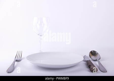 Vuoto piastra bianca, forcella, coltello, cucchiaio vuoto e bicchiere di vino, isolato su sfondo bianco Foto Stock