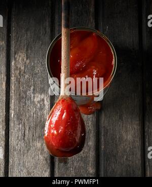 Una lattina di pomodori interi con uno su un cucchiaio di legno Foto Stock