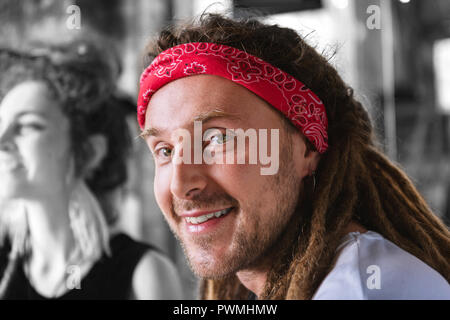 Bel uomo barbuto con dreadlocks indossando red head band sorridente largamente Foto Stock