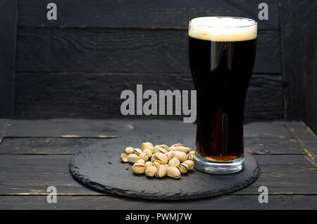 Un bicchiere di birra scura e pistacchi. Un vassoio di ardesia. Un bicchiere di birra. Foto Stock