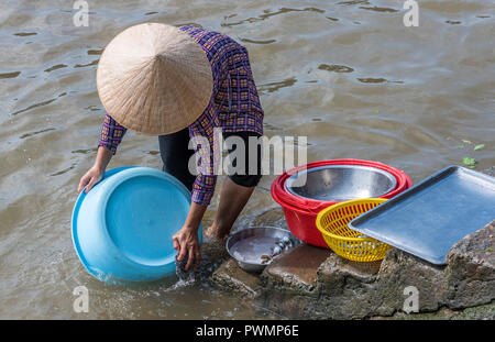 Il Vietnam, il Delta del Mekong, Can Tho, donna con un asiatico cappello conico di lavaggio piatti di lei nel fiume Foto Stock