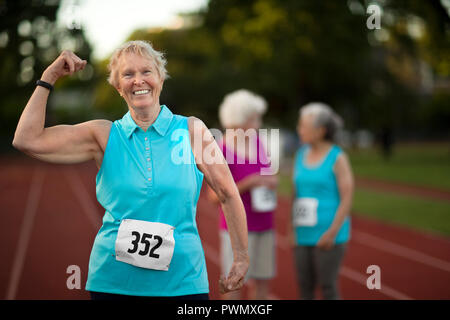 Ritratto di una sorridente donna senior flettendo il suo braccio muscoli. Foto Stock