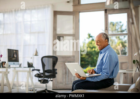 Allegro imprenditore maturo lavora sul suo computer portatile nel suo ufficio di casa. Foto Stock