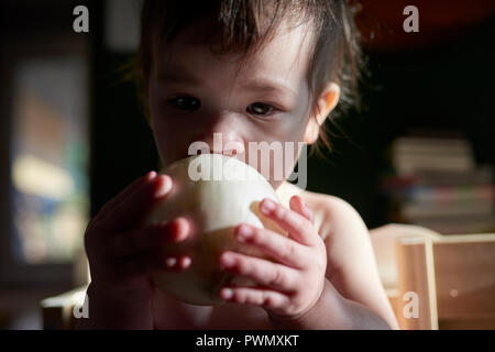 Un anno vecchio toddler girl holding e studiando un grezzo di cipolla in una casa Foto Stock