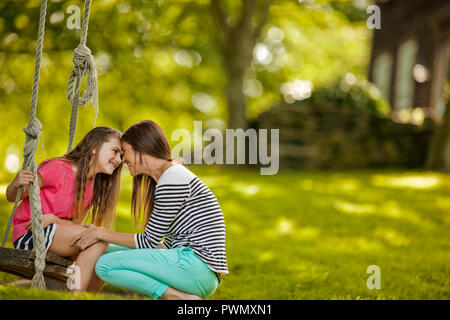 Giovane ragazza seduta su una corda swing trilli affettuosa Madre. Foto Stock