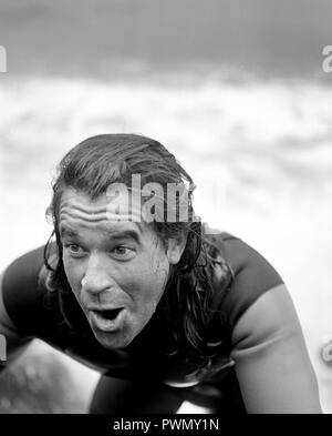 Uomo in wetsuit salendo su rocce dopo arrivare al di fuori dell'acqua. Foto Stock