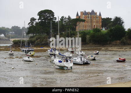 La bassa marea nel piccolo porto con le barche che circonda l'ingresso con questo incredibile caratteristico castello di mattoni rossi e ristorante in Bretagna, Francia Foto Stock