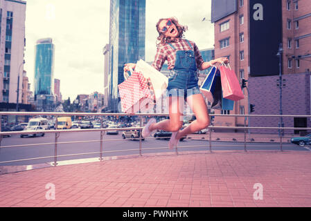 Curly donna che indossa occhiali da sole rosso e bianco sneakers jumping alta Foto Stock