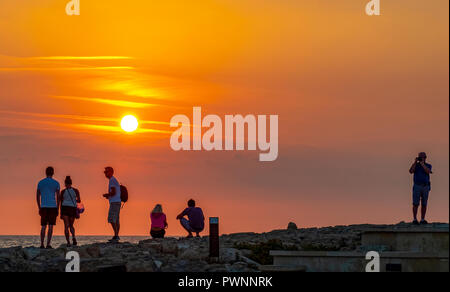 I turisti guardare il sole che tramonta al porto di Paphos, Cipro. Foto Stock