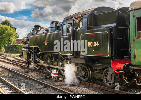 Un treno a vapore che comincia a spostarsi in allontanamento dalla stazione di Corfe nel Dorset come un membro di equipaggio registra l'evento sul suo telefono cellulare. Foto Stock