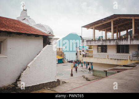 Scuola bambini a giocare giochi con la palla su un cortile della chiesa nel centro di San Juan La Laguna, con vedute del vulcano e del lago Atitlán, Guatemala Foto Stock