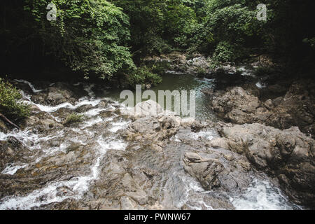 Flusso rocciose si trasforma in cascata che alimenta un verde piscina naturale nella foresta di Montezuma, West Coast Costa Rica Foto Stock