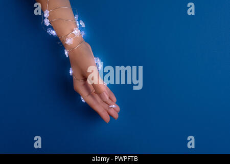 Mano femminile avvolto in forma di fiocco di neve ghirlanda di Natale su carta blu sullo sfondo. Vista dall'alto. Copia dello spazio. Celebrazione di vacanza o per la cura della pelle concept Foto Stock