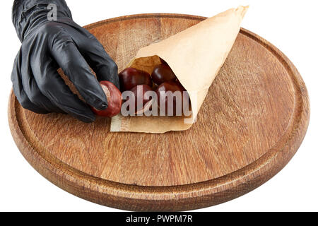 Le castagne e la mano in nero guanto di gomma sulla piastra di legno. Isolato. Foto Stock